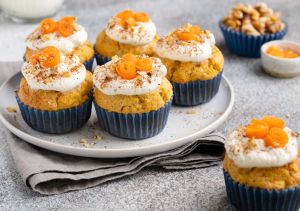 Carrot (pumpkin) cupcakes with nuts and cinnamon. Closeup view of beautifully decorated vegetable muffins with cream cheese frosting, ground nuts, curly swirls of carrot slices.