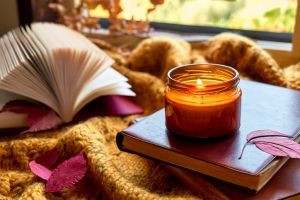 Reading in fall season. Burning candle and open book on knitted plaid with autumn leaves as concept of literature, learning and education in cozy fall mood.