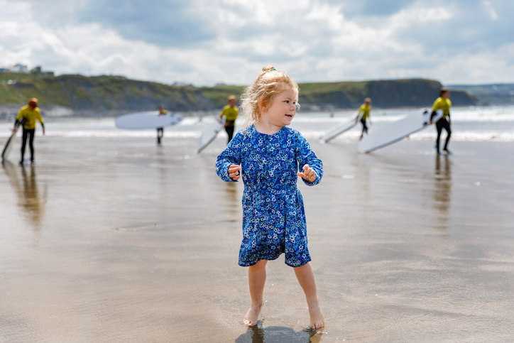 Little cute toddler girl at the Ballybunion surfer beach, having fun on with playing on west coast of Ireland. Happy child enjoying Irish summer and sunny day with family.