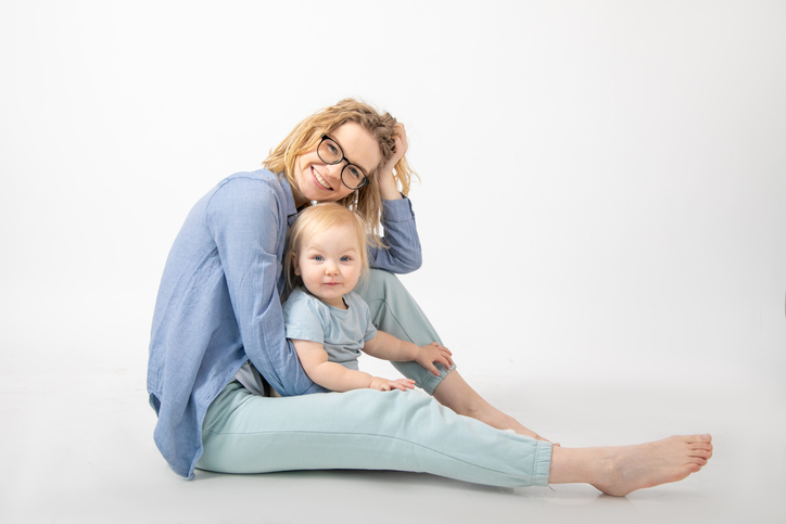 Side view of cheerful family sitting on white background. Young happy woman mother holding little blond blue-eyed girl.