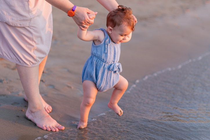 Mother and baby walking on sandy beach. Space for copy.