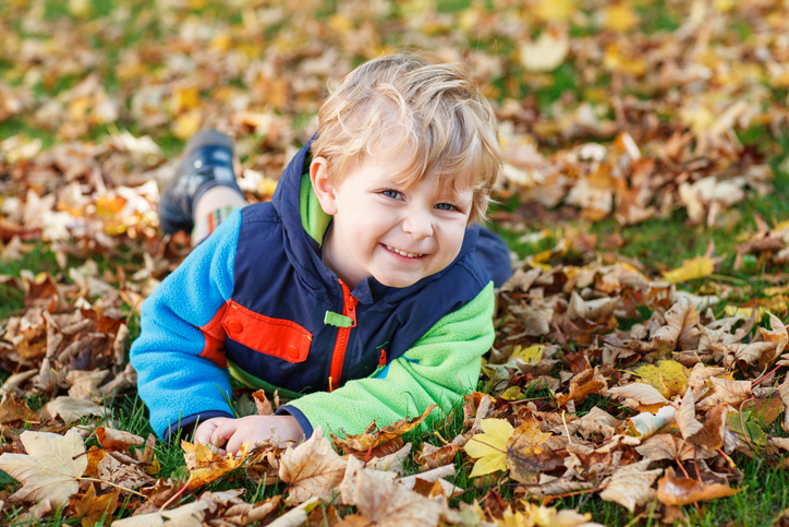 Cute little boy playing with maple leaves outdoors. Happy child walking in autumn park. Toddler baby boy wears trendy jacket . smiling Blonde boy portrait. Autumn fashion. Stylish child outside.