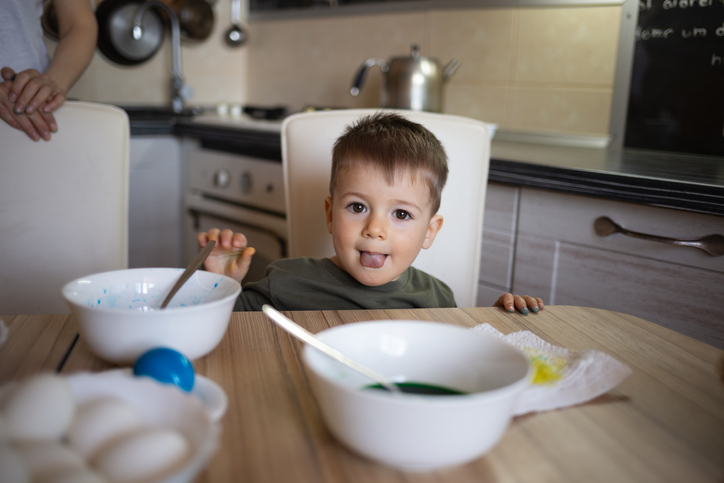 little cute boy paints eggs for easter sitting in the kitchen at the table