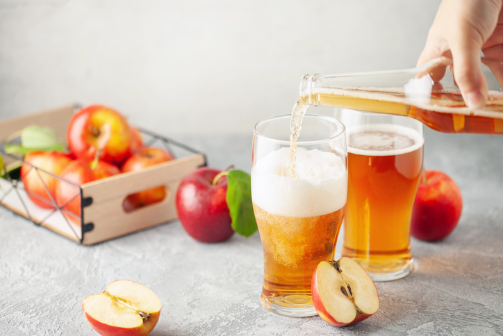 Boozy Refresing Cold Hard Apple Cider in a Pint Glass and Bottle on wooden table. Copy space