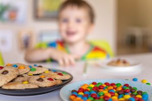 Funny boy eat cookies with round multi-colored sweets m&m and drink milk