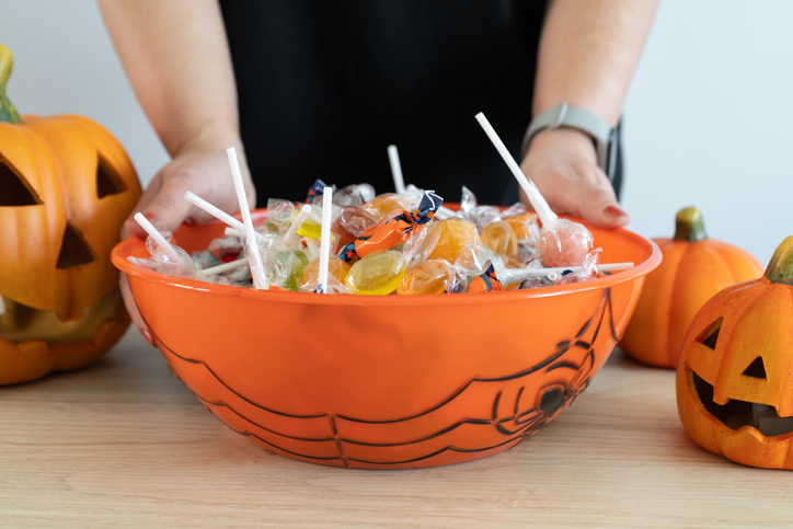 Woman holding a Halloween candy bowl filled with sweets for trick-or-treating.