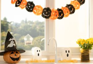 Halloween concept. A pumpkin with a painted face, a white ghost and a bouquet of yellow chrysanthemum flowers in a black vase against the background of a window in home interior.