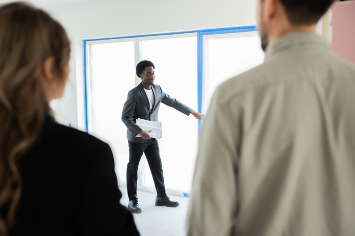 Picture of a focused, busy, dark-skinned African American real estate agent standing inside the new home and showing prospective clients and consumers every aspect