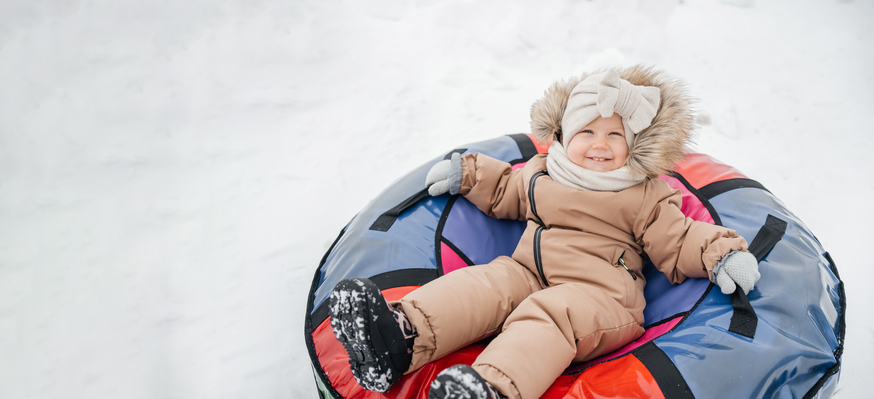 joyful child riding in the snow on snow tube