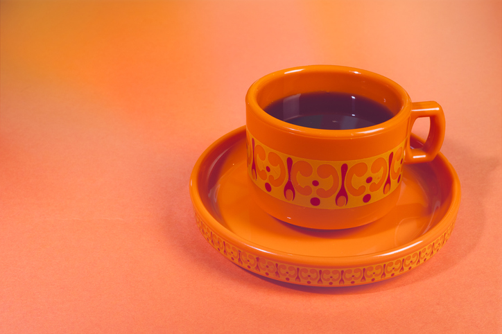 Vintage-Inspired Orange Cup and Saucer Set with Delicate Scrollwork Design on a Peach-Colored Surface