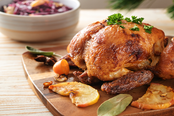 Festive roast chicken fresh from the oven with apples, kumquat, spices and herbs served with red cabbage on a wooden table, poultry dinner for Christmas or Thanksgiving, copy space