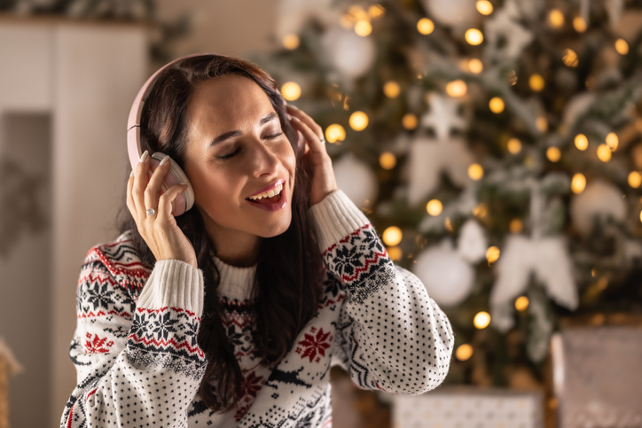 Satisfied brunette listens to music through headphones and sits at home in front of the Christmas tree.