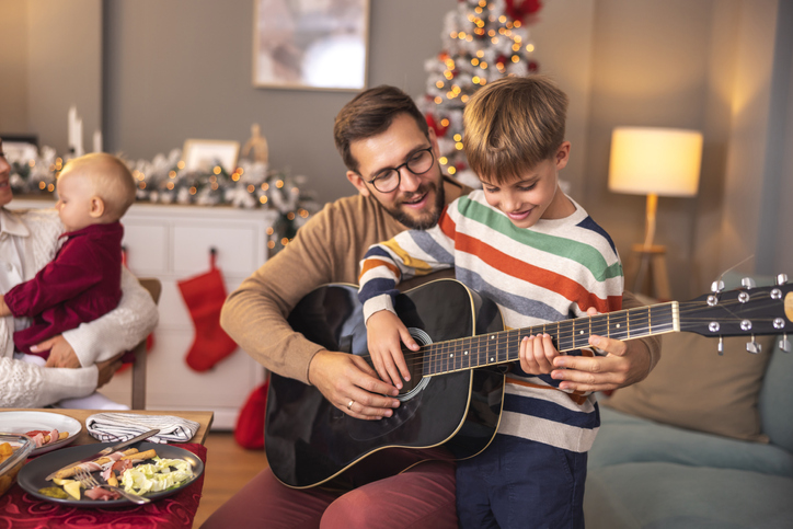 Father teaching son to play the guitar while having Christmas dinner at home