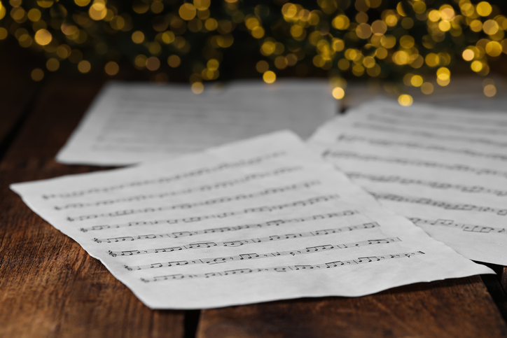 Closeup view of note sheets on wooden table against blurred lights. Christmas music