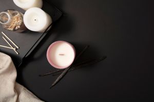 Two white candles and a bottle of cotton swabs are displayed on a black tray. A jar of scented candles is placed on the table with a black background. Candle advertisement with minimalist background.