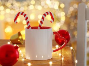 Red and White heart shaped handle coffee cup with ornaments sitting on a wooden table in a Christmas scene