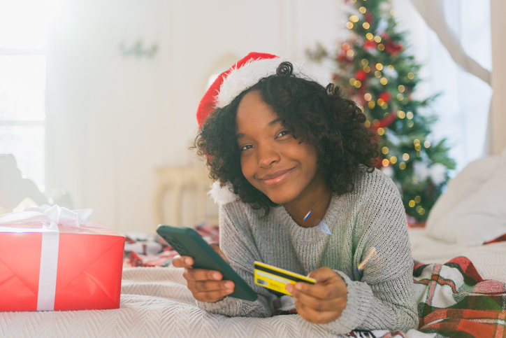 African American woman shopping online holding smartphone paying with gold credit card for Christmas gifts, Girl buying on Internet enter credit card details enjoying Christmas winter holidays at home