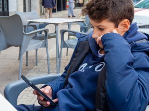 Modern childhood: Boy dressed in blue, distracted with his smartphone on a busy street.