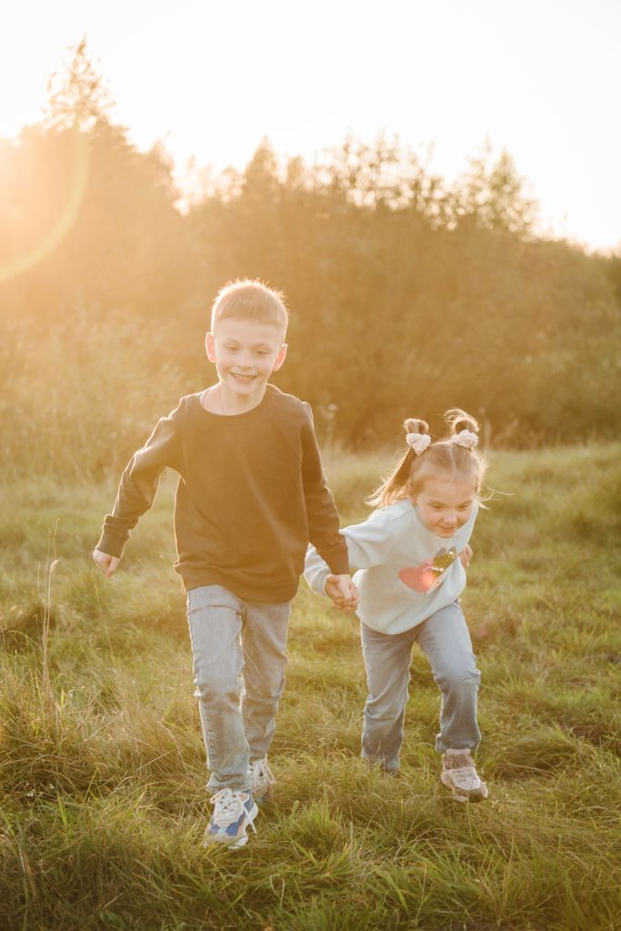 Happy children walking spending time together in nature. Daughter, son hold hands and run in green grass in field at sunset. Concept family holiday outdoors. Kids playing in mountains on autumn day.