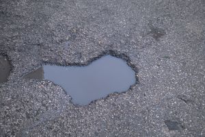 A water-filled hole on an asphalt street. It poses a danger to pedestrians, motorcycles and vehicles.