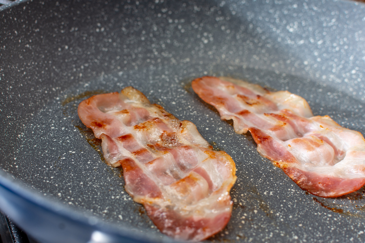 Two pieces of bacon are fried in a pan