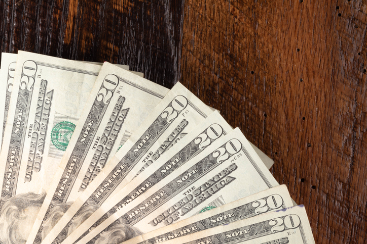 United States currency, twenty-dollar bills fanned out on a wooden background.