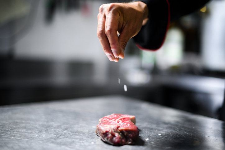 Chef pouring salt on a raw steak to season it