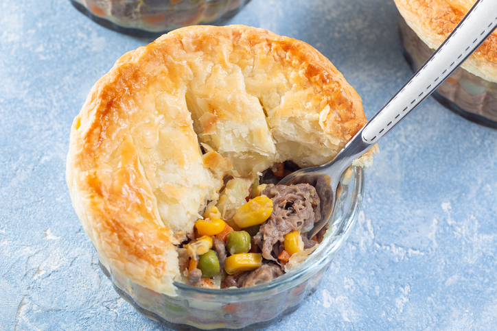 Individual beef pot pie or deep dish pie in ramekin, crust broken open to show inside, horizontal