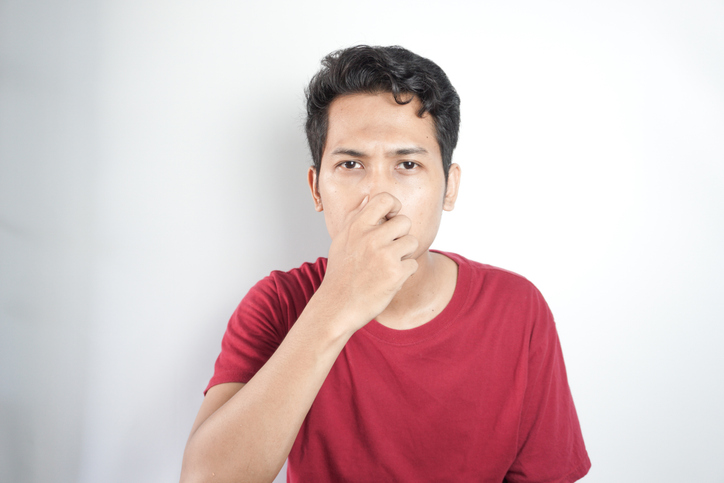 disgusted asian young man covering nose with hands