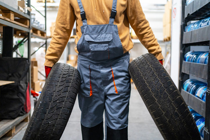 Unrecognisable warehouse worker carrying tires at storage room