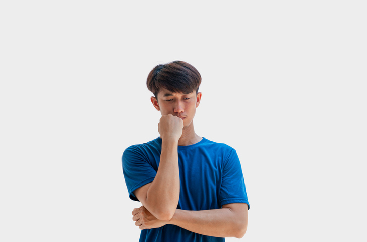 A young Asian man in his 20s wearing a blue t-shirt standing thinking isolated on a gray background. A man stressed out by problems going through life. tension concept