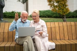 Active seniors using laptop outdoor and paying online bills with credit card