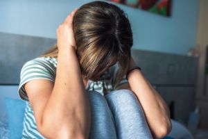 Young woman covering her ears with her two hands sitting on a bed in a room. Concept of anxiety