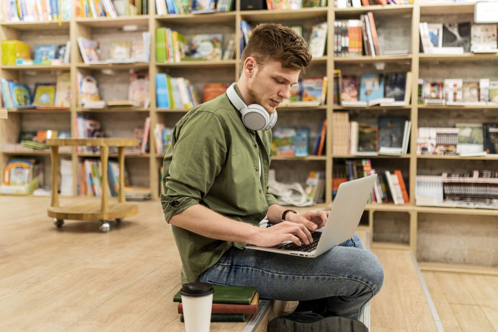 Student Immersed in Reading at Library Using Laptop