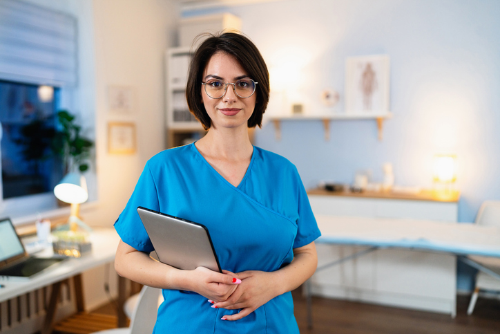 Portrait of a young Caucasian female doctor in blue medical scrubs, holding digital tablet