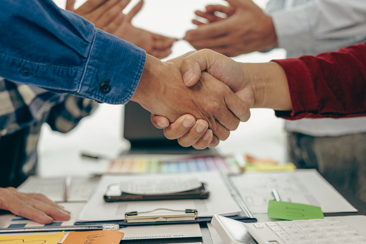 Young business people shaking hands and meeting with documents above to hire a partner or work together at the office, teamwork or researching a new marketing project in close-up.