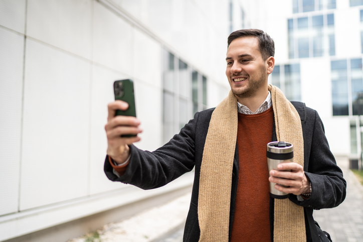 Young businessman holding smart phone for business work and drink coffee to go on break.