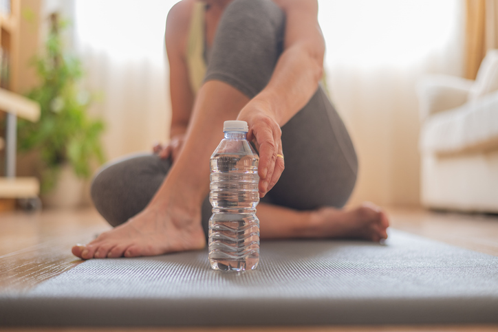 Close-Up of a Woman Holding a Water Bottle on a Yoga Mat.