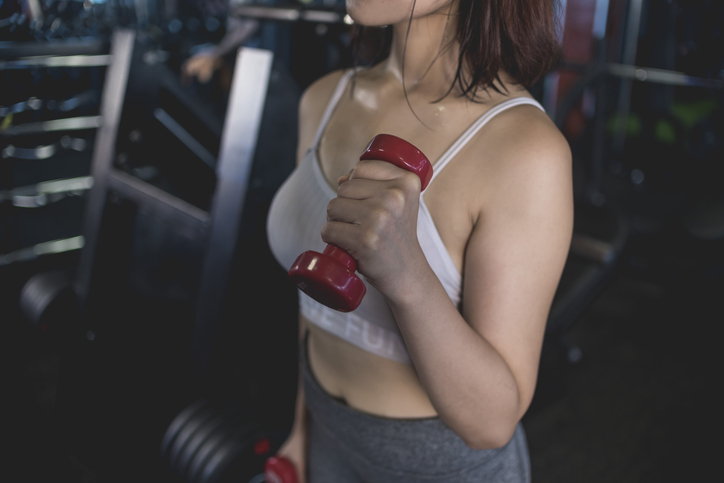 An anonymous woman doing a set of alternating hammer bicep curls at the gym.