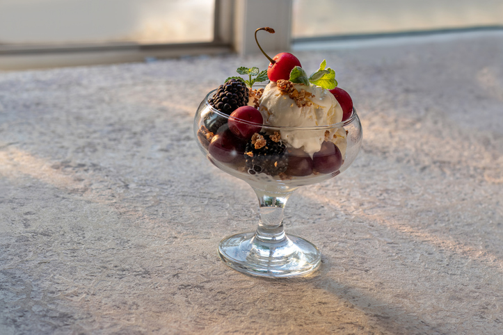 Ice cream with blackberries and cherries in glass ice cream bowl.