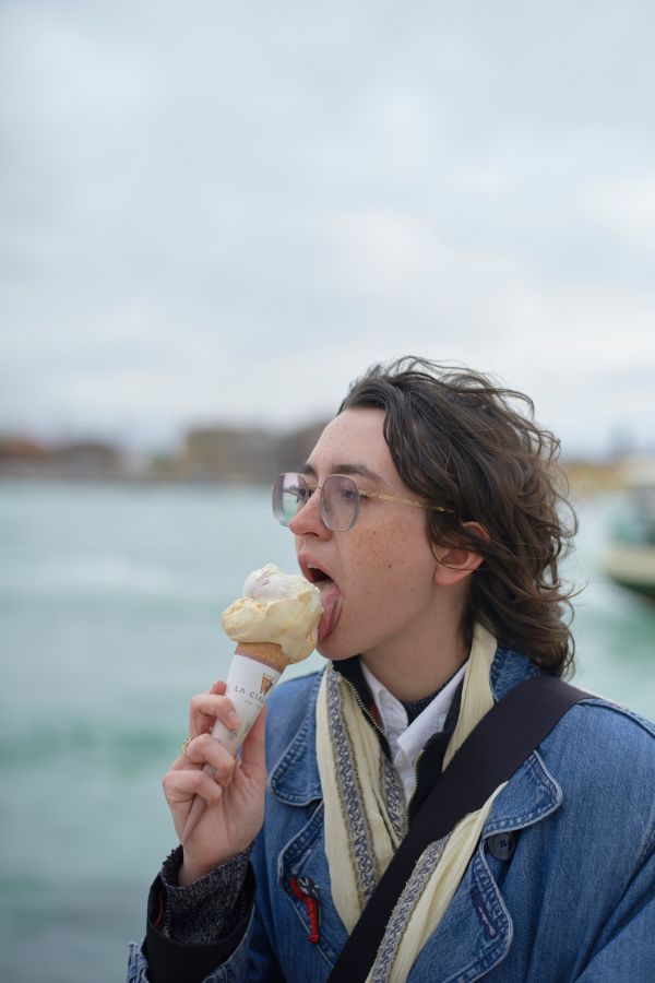 Young adult enjoying an ice cream cone by the water with boats in the background