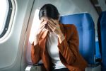 A young Asian woman, an airplane passenger, sits by the window seat, experiencing nausea and dizziness during the flight, which adds to her travel discomfort.