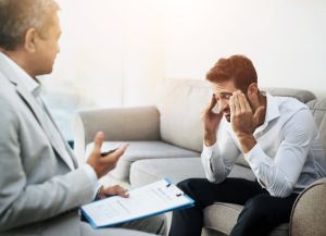 PTSD, psychology or trauma with counsellor and patient in office of hospital for grief, loss or pain. Depression, stress and therapy with man talking to mental health doctor for counseling or rehab