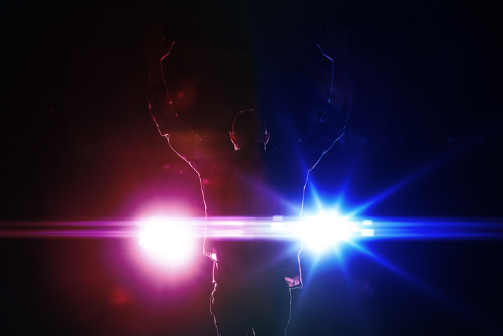 silhouette of a male criminal suspect with hands up during night pursuit in front of the police car headlights