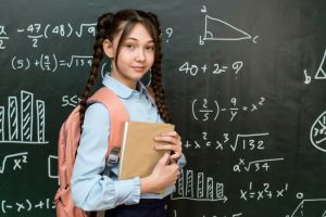 A high school schoolgirl stands near the blackboard with a textbook in her hands, portrait of a teenage girl at school