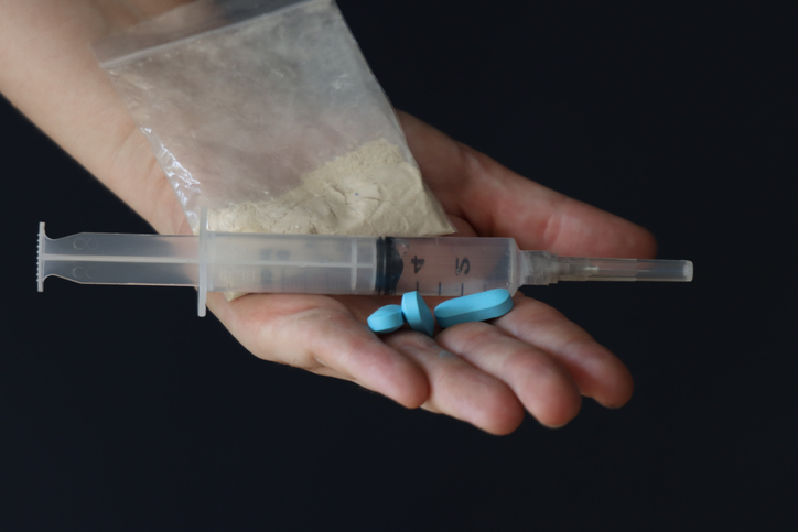 Woman holding a pack with drug powder, pills and syringe to illustrate the drug addiction