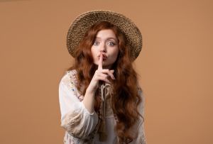 Gossiper pretty woman with finger on lips - shh, secret, silence, hush on beige