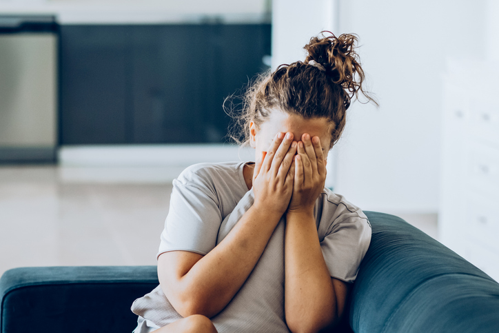 Woman sitting on the sofa and covering her face with her hands.
