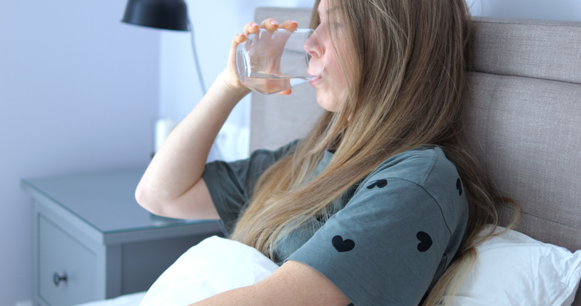 Lady drinks water and puts glass onto bedside cabinet sitting in comfortable bed