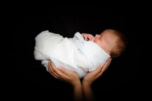 Cropped Hands Of Parent Holding Newborn Baby Against Black Background